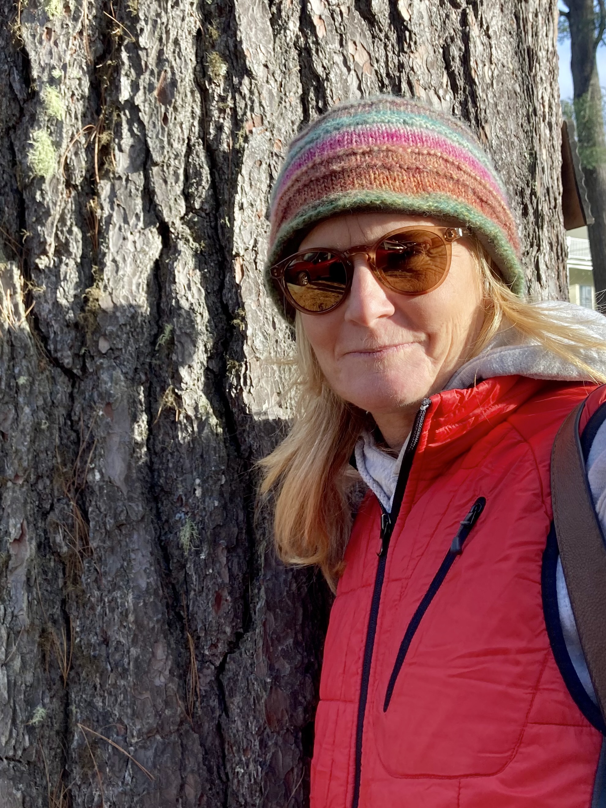 woman leaning against tree with sunglasses and striped hat